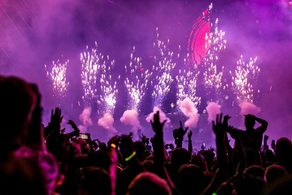 Vibrant EDM concert scene with fireworks, smoke, and enthusiastic crowd enjoying the music.