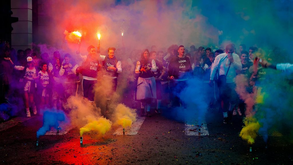 A lively group celebrating at night with color smoke bombs in a street festival.